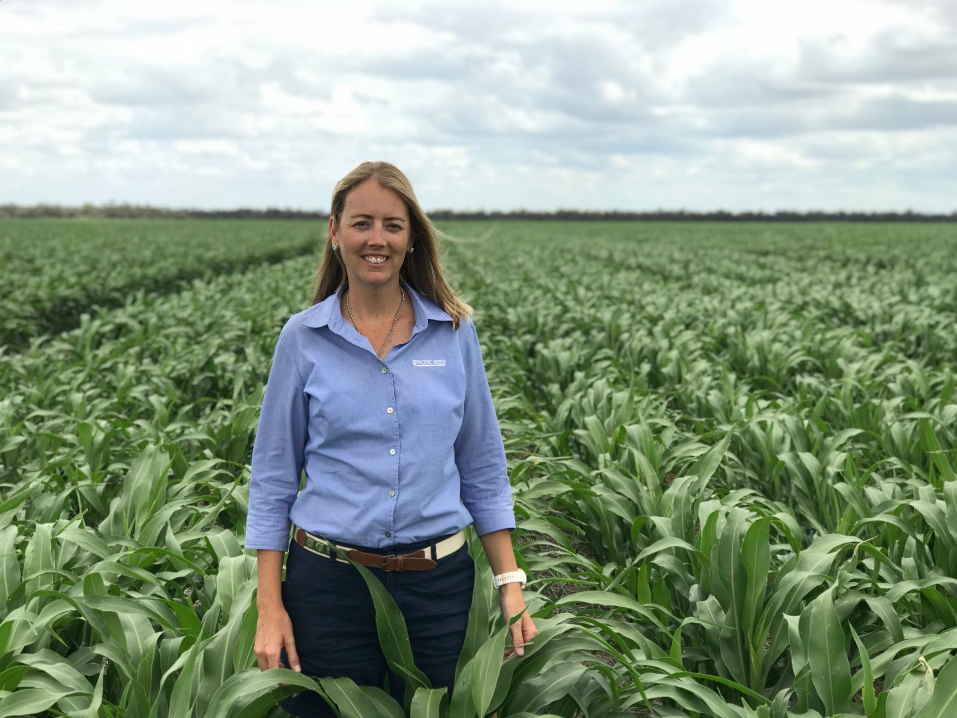 Woman standing in a lush green crop field under a cloudy sky