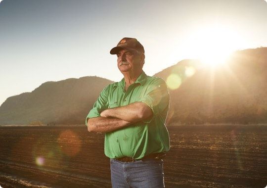 Man standing with arms crossed in a green shirt at sunset, with mountains in the background