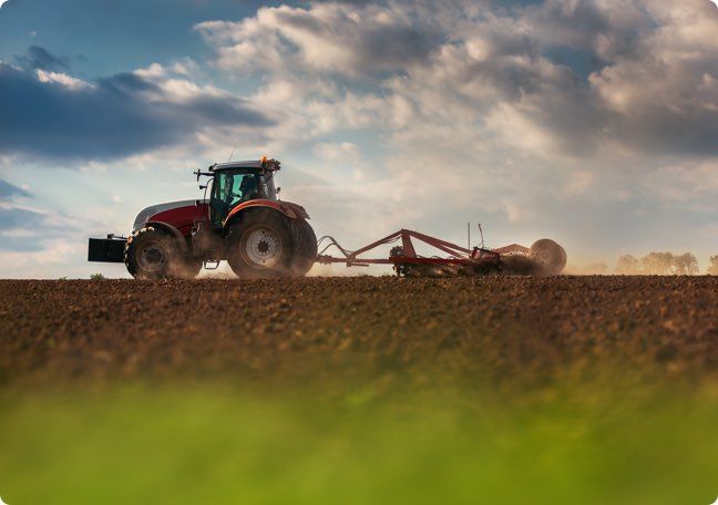 Red tractor plowing a field under a cloudy sky at sunset