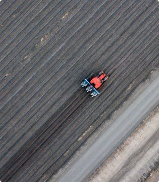 A red tractor plows a dark field in diagonal rows.