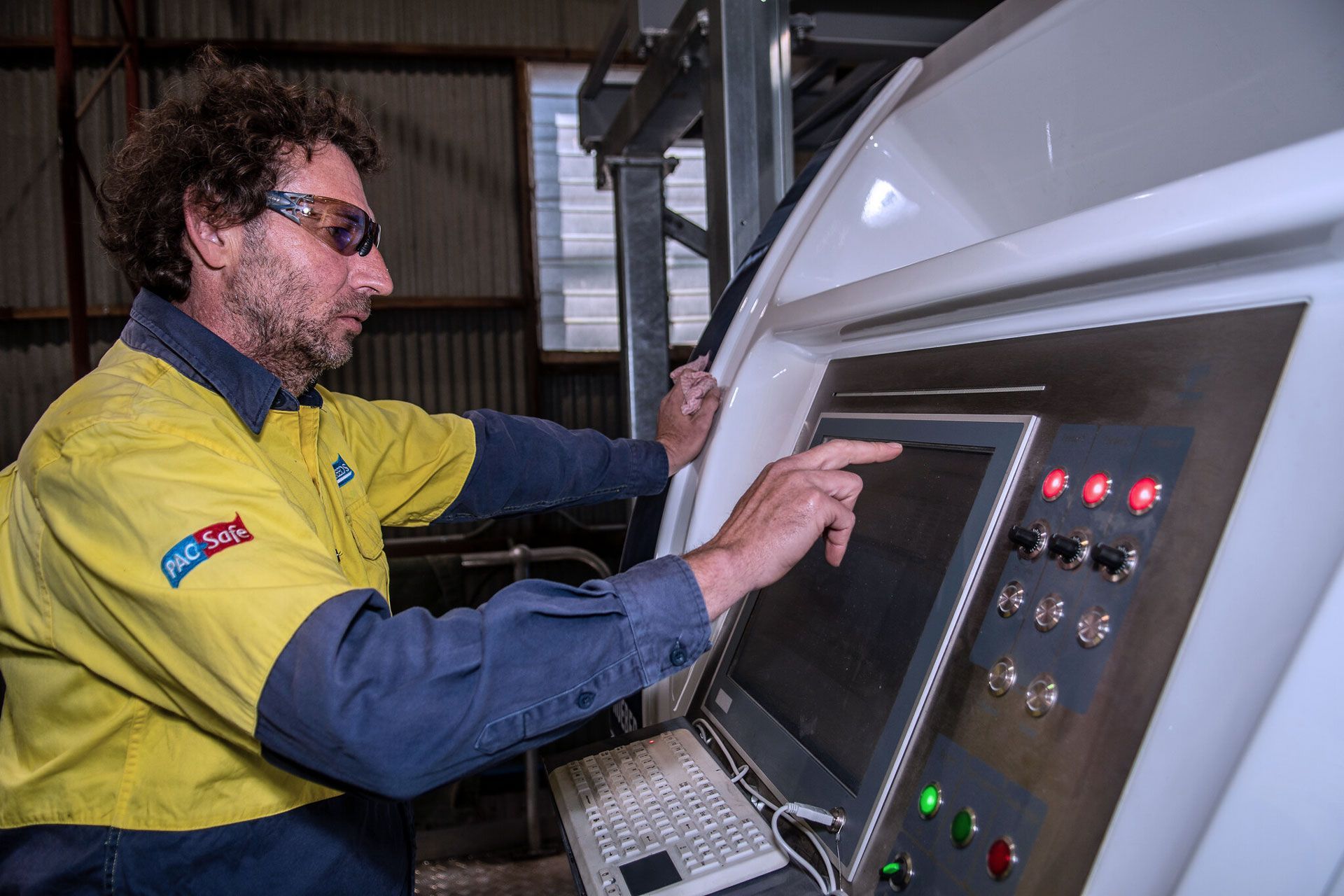Technician in yellow jacket using a touchscreen control panel beside a large industrial machine.