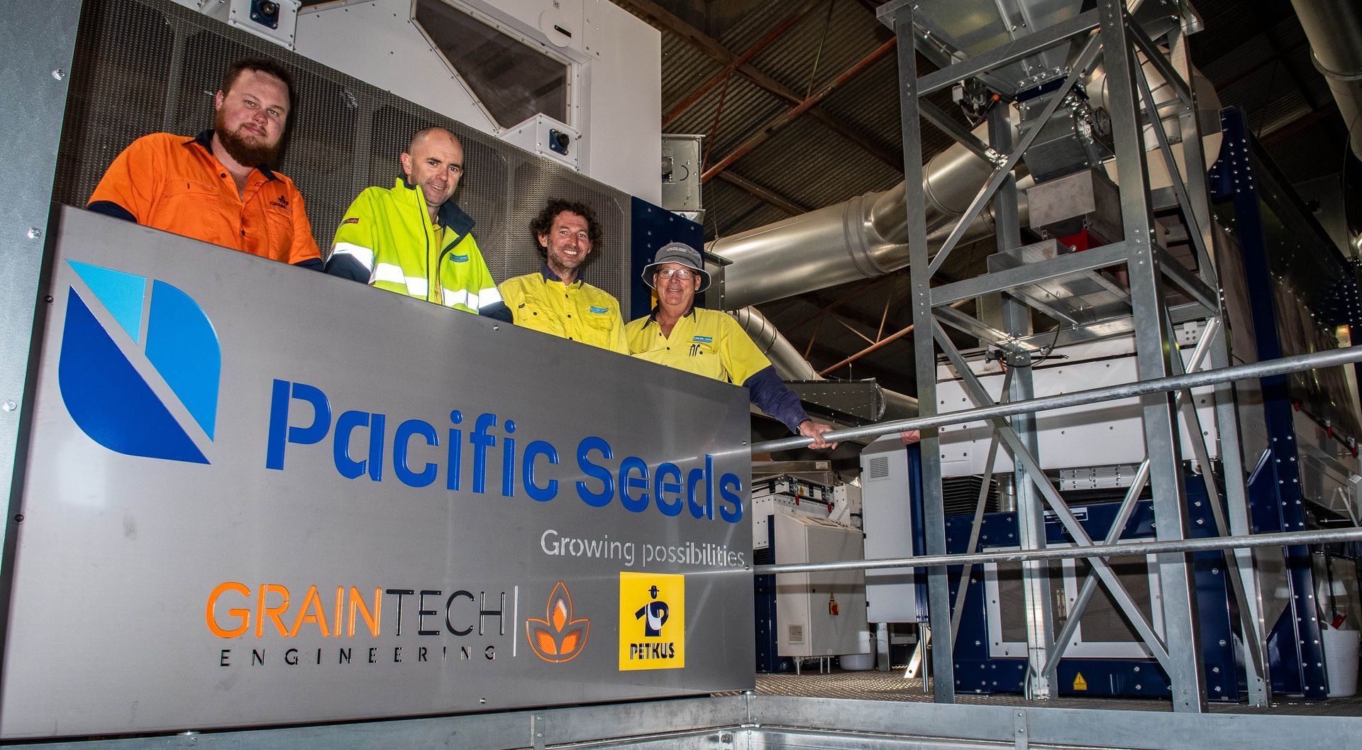 Workers on a construction platform beside a Pacific Seals sign and industrial piping within a steel structure