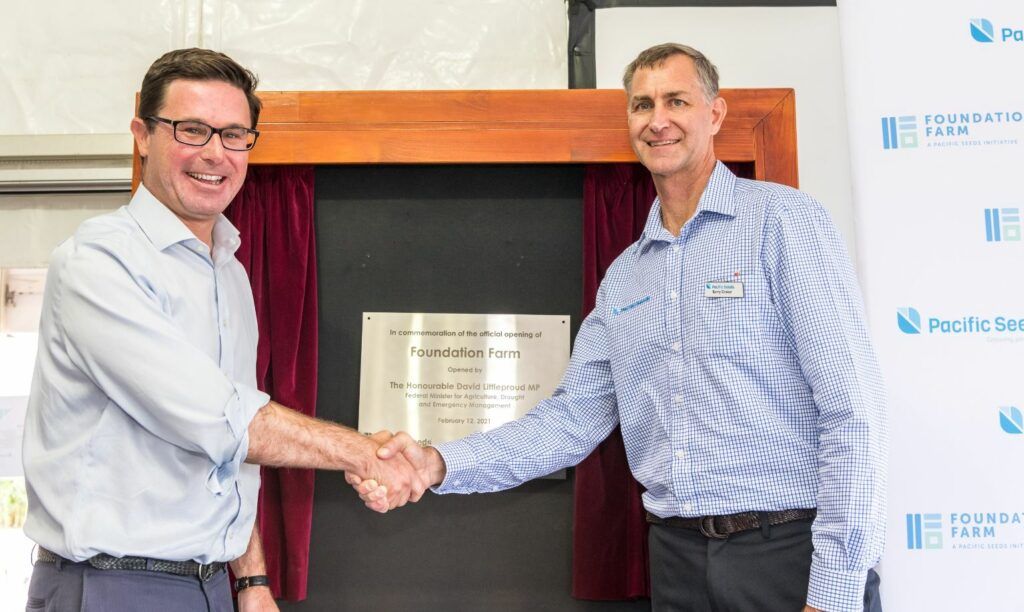 Two men in dress shirts shake hands in front of a ceremonial fireplace unveiling display.