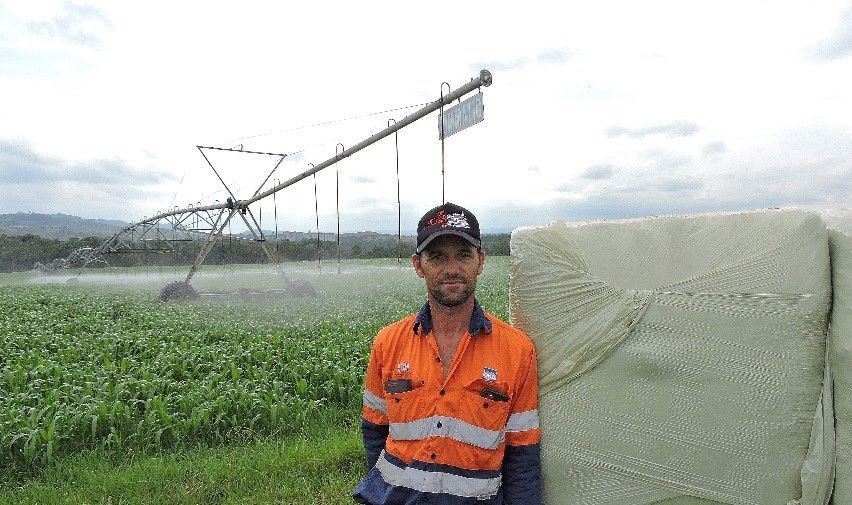 Worker in orange safety gear stands beside irrigation equipment in a green field.