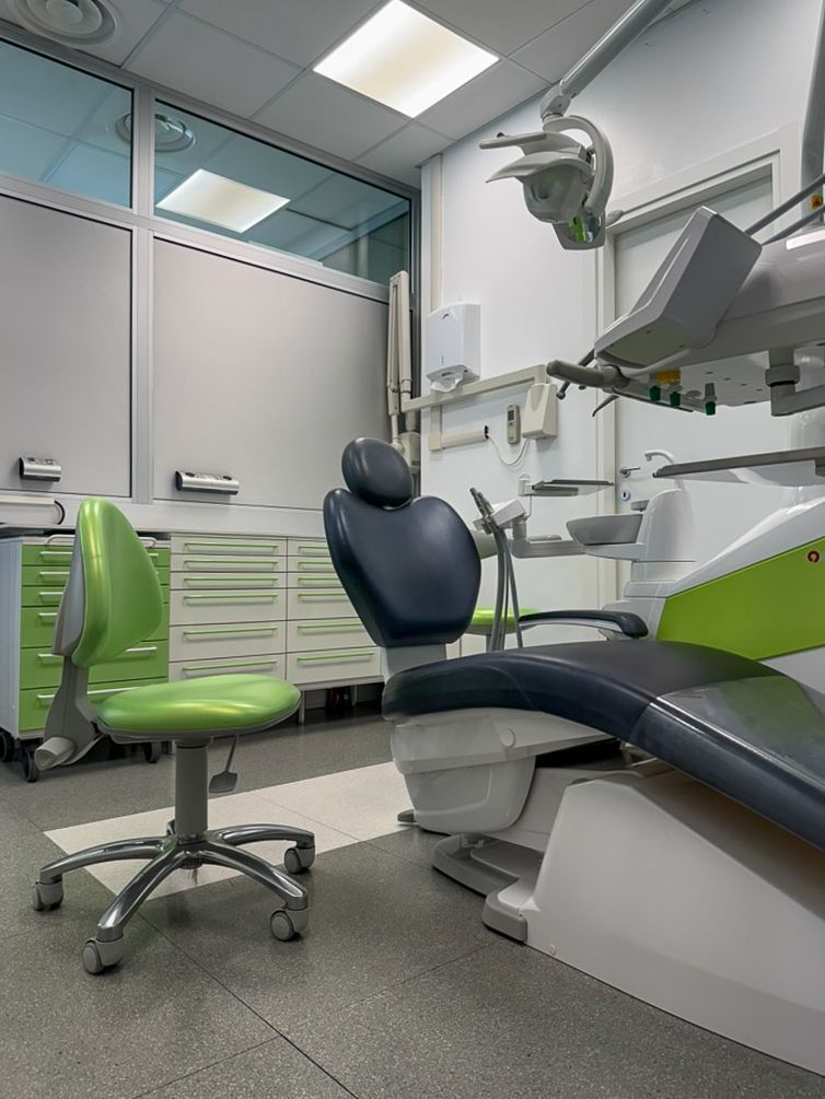 Clinica odontoiatrica moderna con poltrona, lampada a soffitto e sedie d'attesa verdi in una stanza sterile.