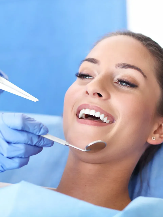 Un dentista esamina un paziente sorridente con uno specchio e uno strumento odontoiatrico in un ambiente clinico blu.