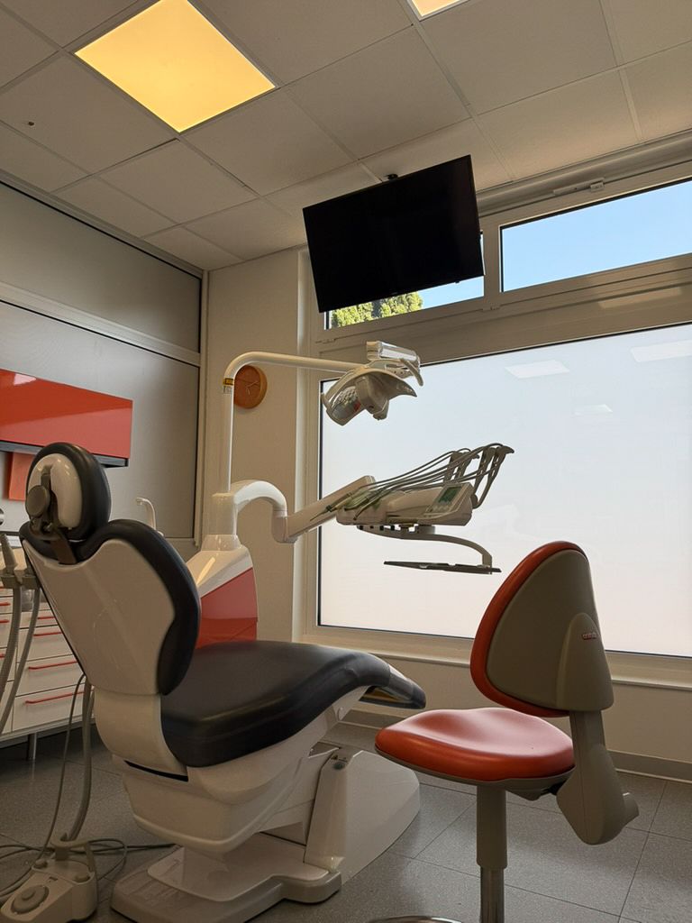 Sala per visite odontoiatriche con poltrona reclinabile, lampada a soffitto e monitor accanto a una finestra.