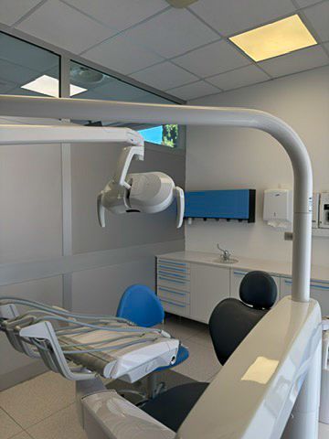 Sala per visite odontoiatriche con poltrona reclinabile, lampada a soffitto e armadietti sotto luci fluorescenti.