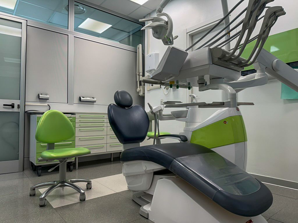 Clinica odontoiatrica moderna con poltrona, apparecchiature aeree e armadietti verdi.
