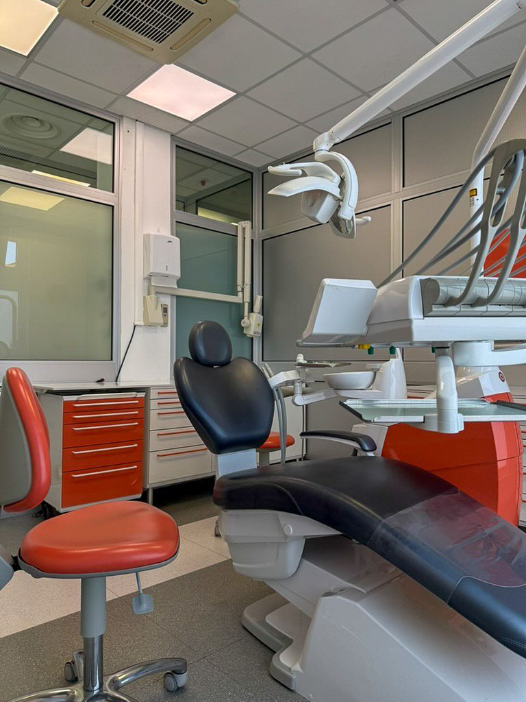 Sala visite odontoiatriche vuota con sedia nera, sgabello rosso e luci a soffitto.