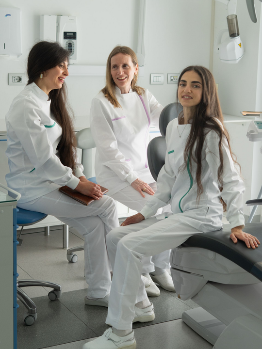 Un professionista sanitario è seduto in una luminosa sala visite, accanto a una poltrona e alle relative apparecchiature.