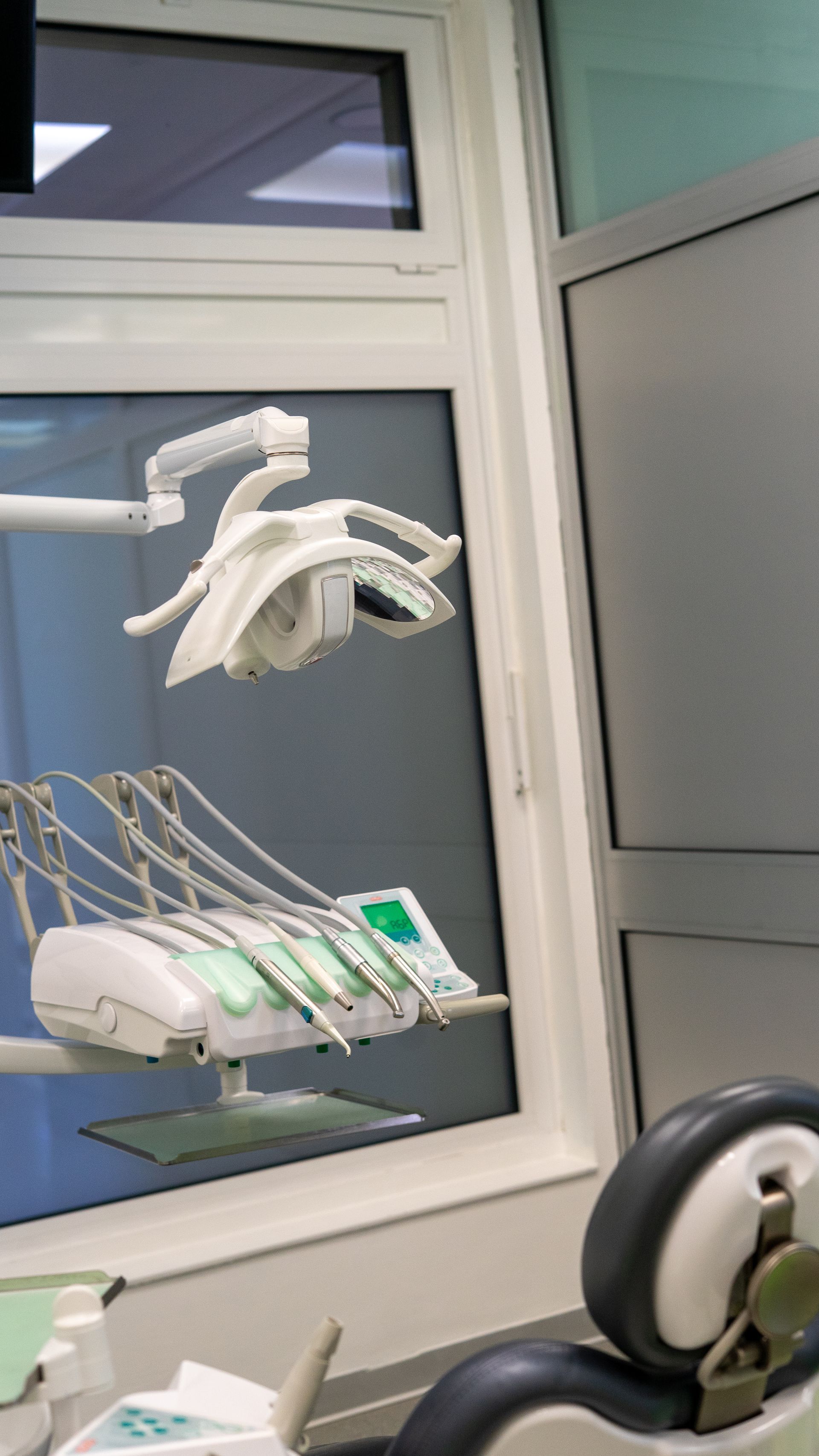 Poltrona da studio dentistico con lampada odontoiatrica sopraelevata e strumenti posizionati vicino a una finestra.