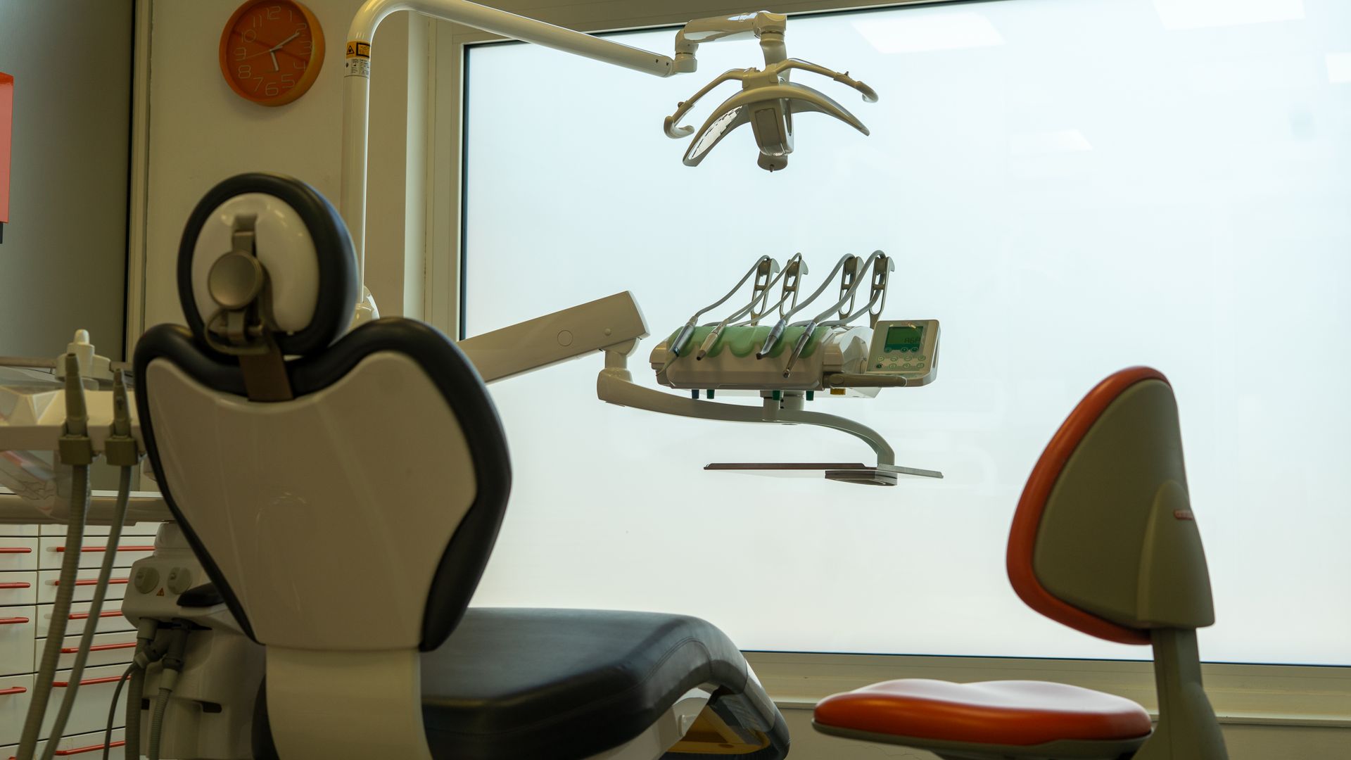 Sala visite odontoiatriche con sedie, luci a soffitto e attrezzature posizionate di fronte a una finestra luminosa.