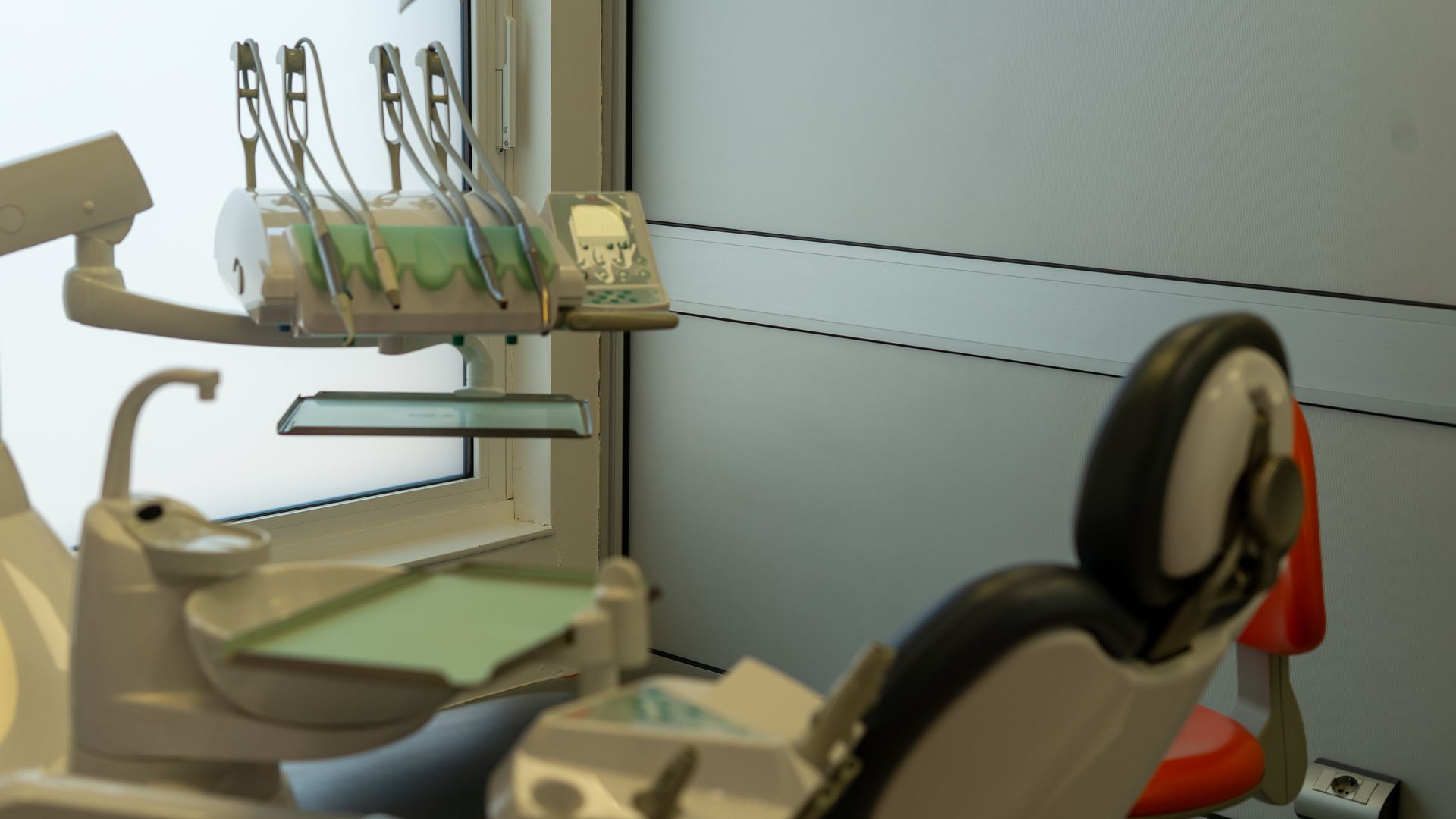In una sala ambulatoriale, una poltrona da dentista è posizionata accanto a una mensola a muro con strumenti e un monitor.