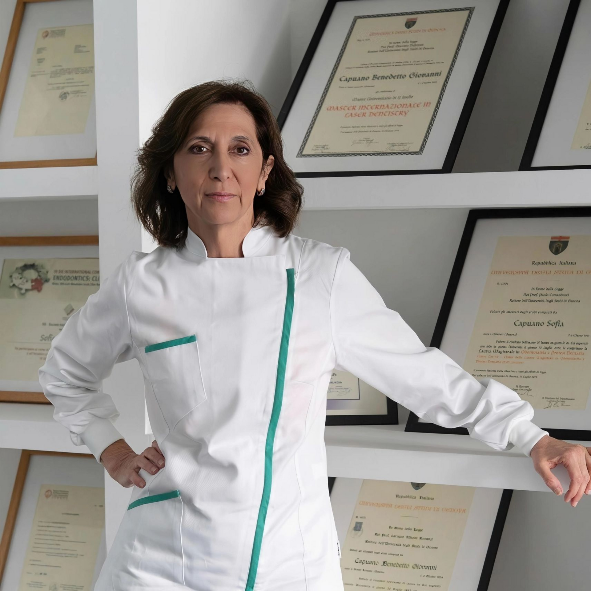 Una donna in uniforme bianca è in piedi in un ufficio, con certificati incorniciati appesi alla parete.