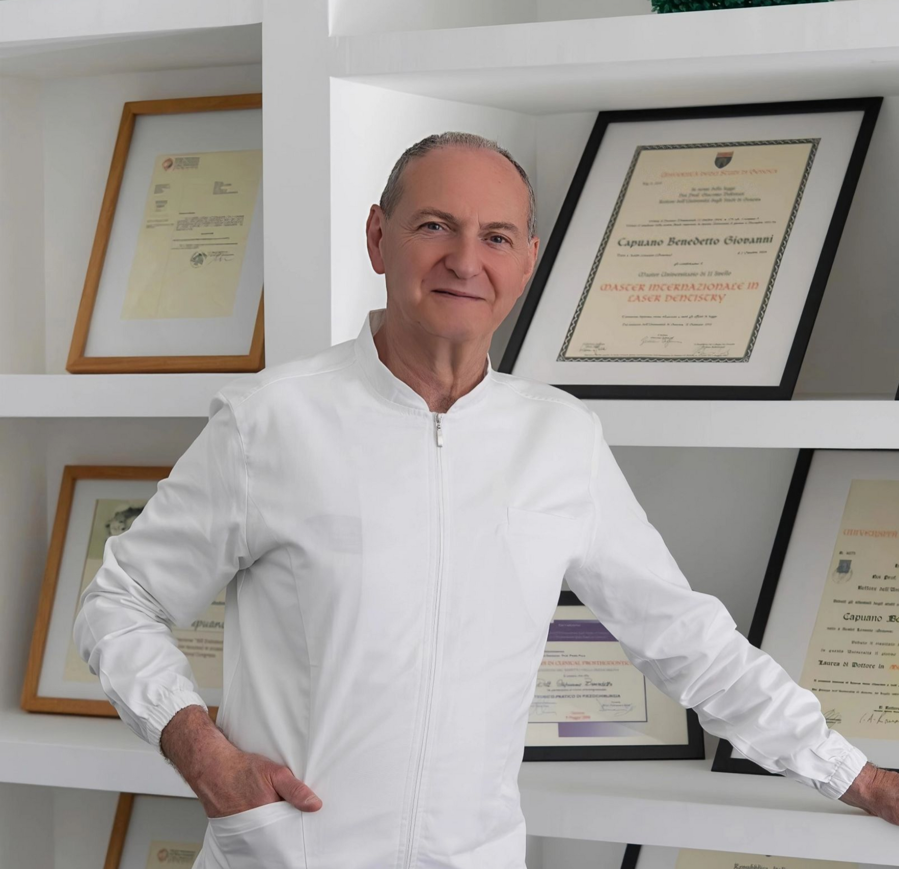 Un uomo con una camicia bianca è in piedi davanti a degli scaffali su cui sono esposti certificati incorniciati.