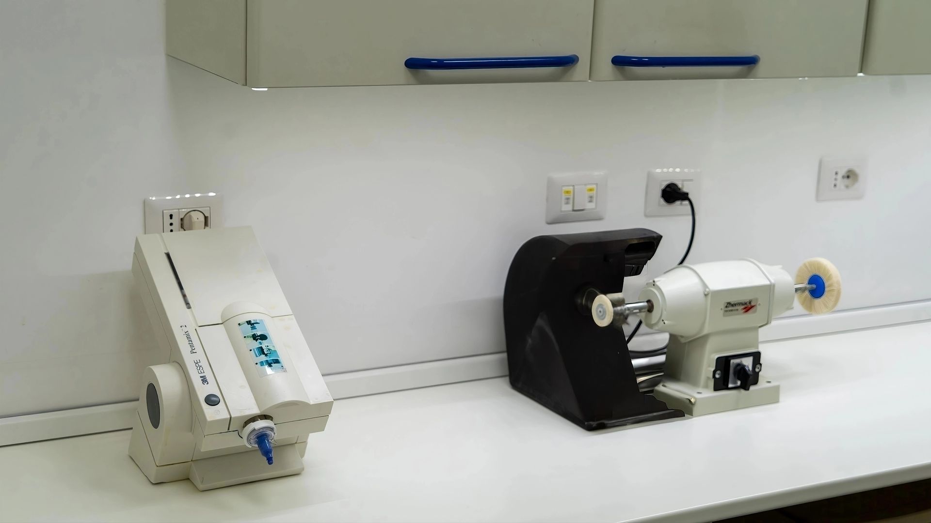 Banco da laboratorio con due macchine da banco bianche e una camera metallica aperta tra di esse.