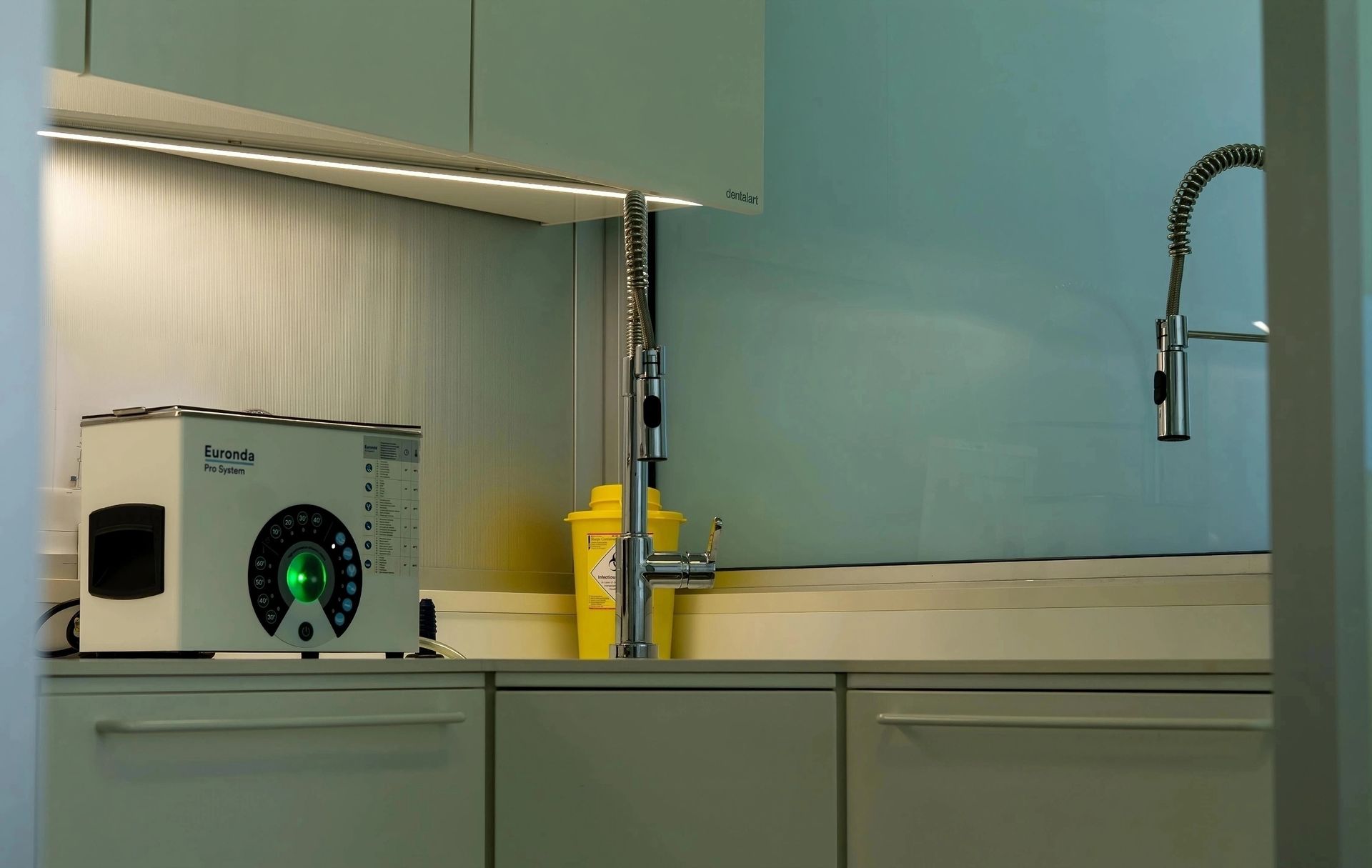 Cucina moderna con mobili chiari, lavello, rubinetto e piccoli elettrodomestici sul bancone.