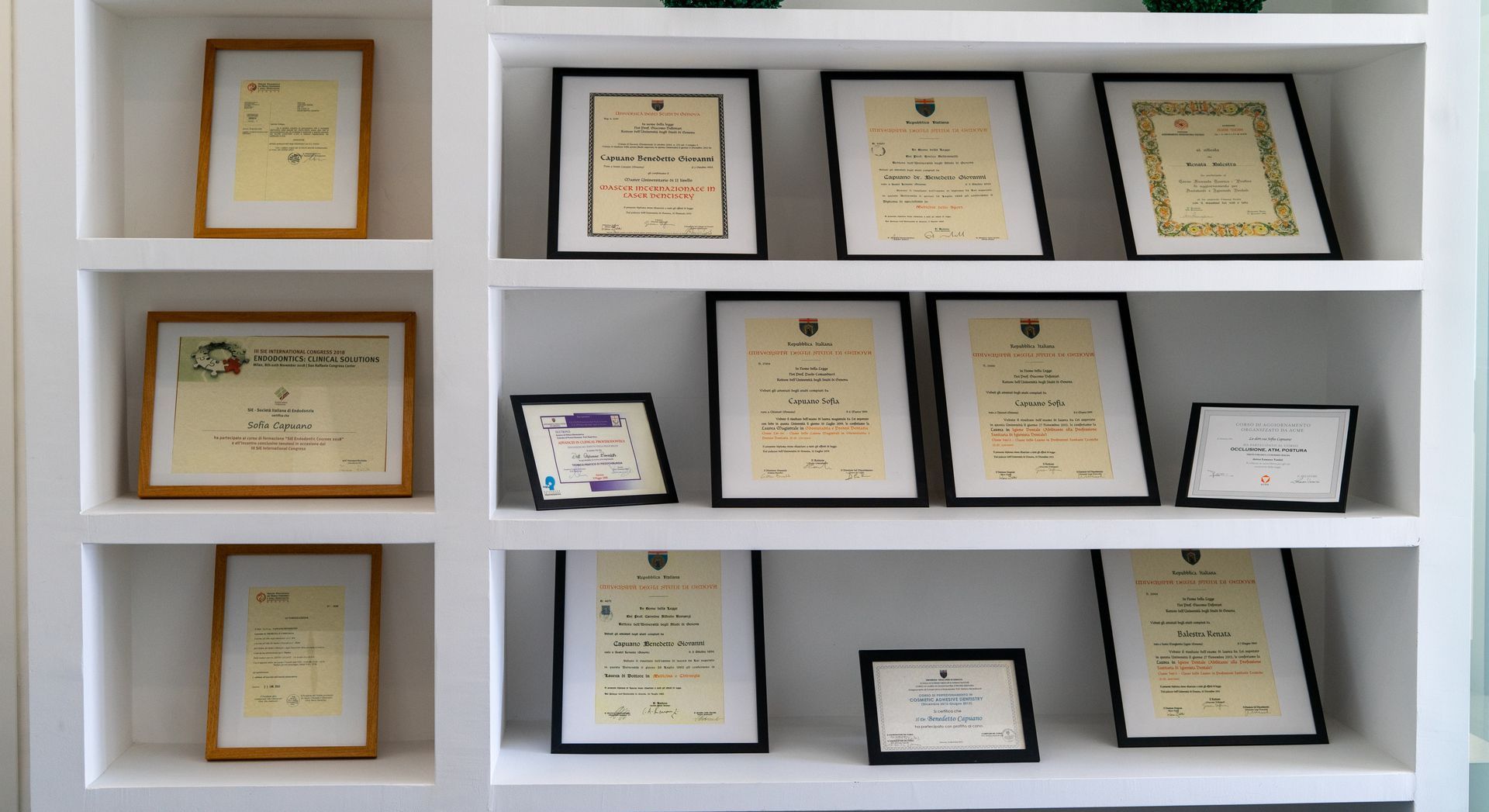 Mensole bianche che espongono certificati e premi incorniciati in un ambiente domestico o in ufficio.