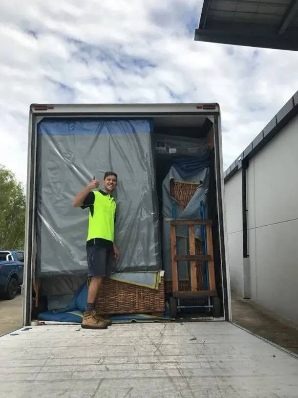 A removalist is standing on the back of a truck smiling — O'Grady's Transport & Removals in Yamba, NSW