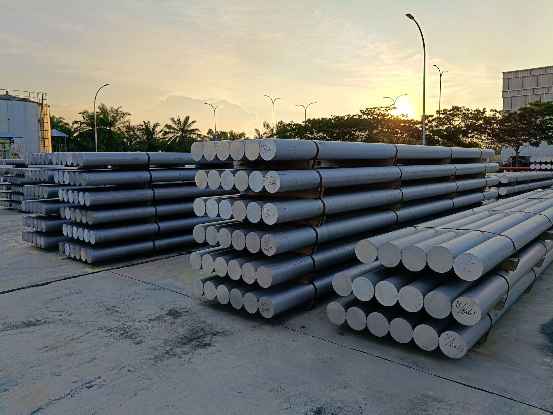 Stacks of large steel pipes piled in an industrial yard at sunset.