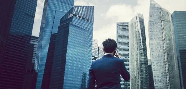 Person in a suit looking up at tall glass skyscrapers in a modern city skyline