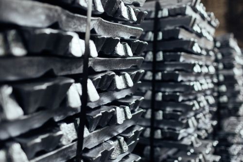 Stacks of dark metal ingots or bars arranged in rows in an industrial storage area