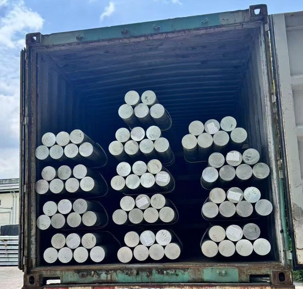 Open shipping container packed with stacked white cylindrical pipes or logs.