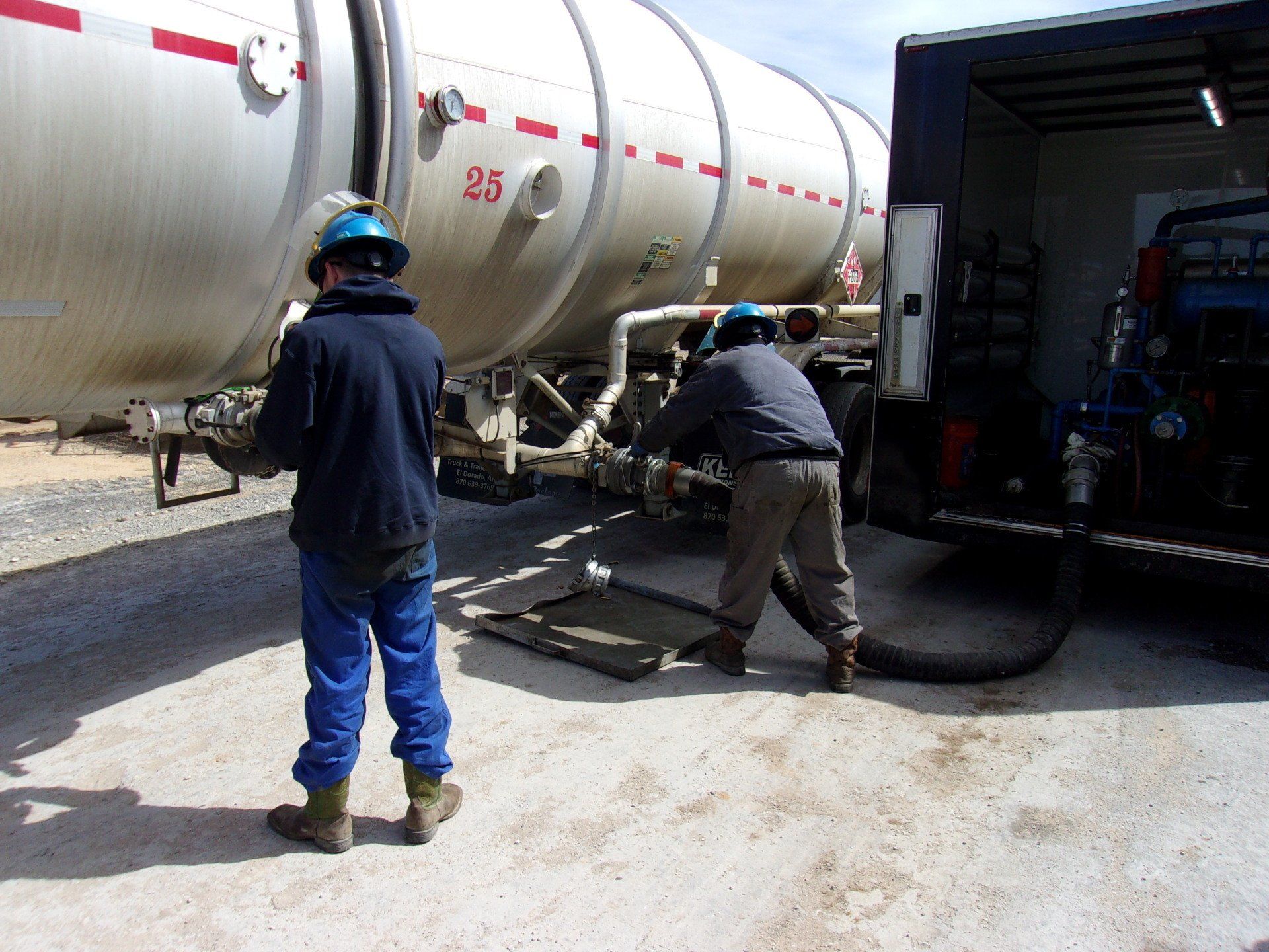 Two men are working on a large tank with the number 23 on it