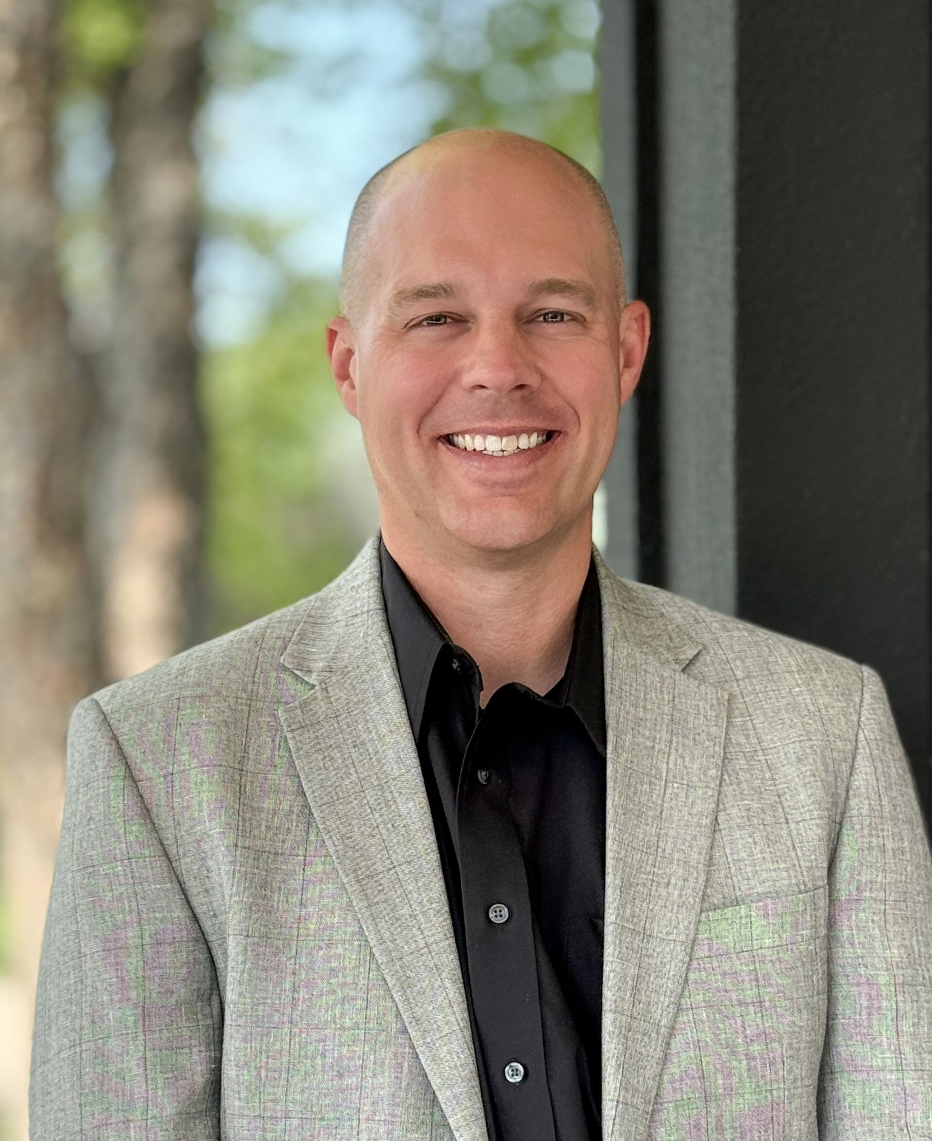 A man in a suit and black shirt is smiling for the camera.