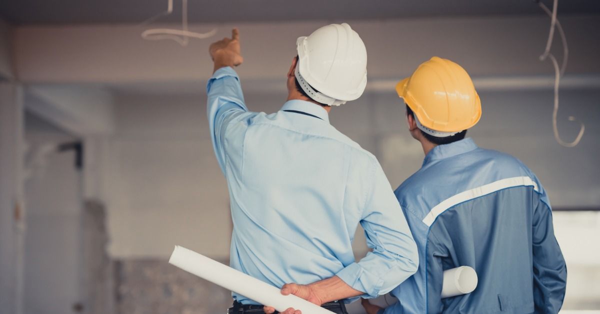 Two professionals wearing hard hats and holding rolled up documents on a construction site. One pro
