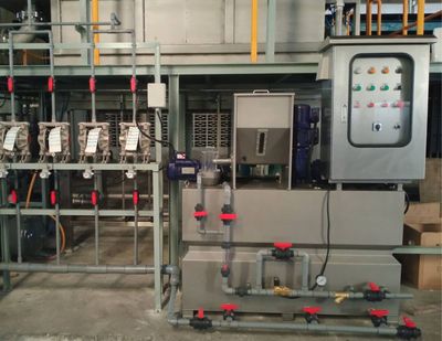 Industrial water treatment system with pipes, valves, pumps, and a control panel in a factory room