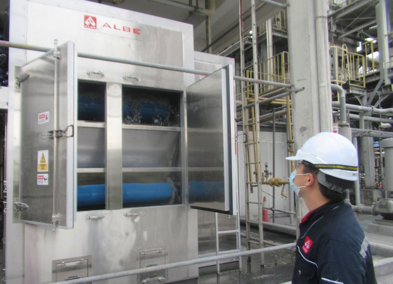 Worker inspecting a large industrial machine with open doors and blue rollers in a factory
