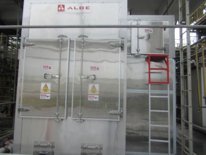 Large industrial metal chamber with double doors, warning signs, and a red ladder in a factory setting