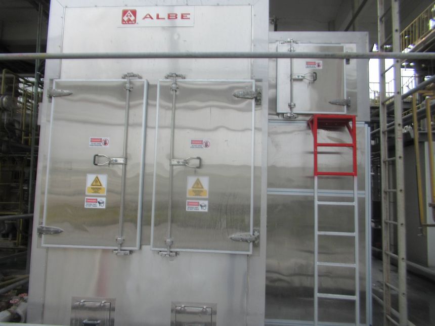 Large industrial machine with metal doors, warning signs, and a ladder in a factory setting