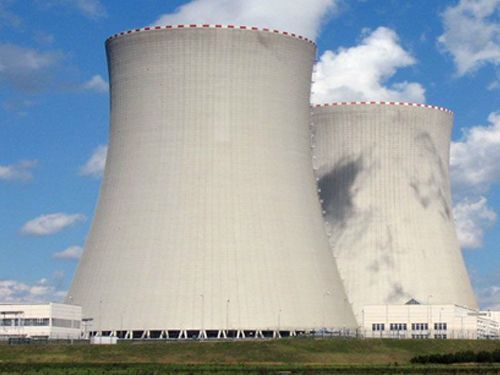 Two large white cooling towers at a power plant under a blue sky with clouds