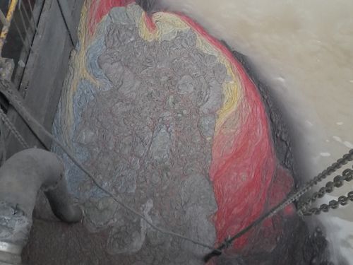 Large gray rock-like mass with red-painted edges wedged in a narrow industrial shaft with chains.