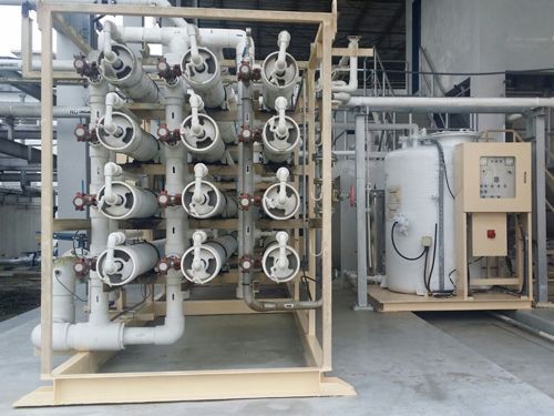 Industrial water treatment system with multiple white valves and pipes mounted on a metal frame in a factory.