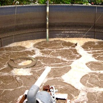 Circular wastewater tank with brown churning sludge and white foam around a central pipe
