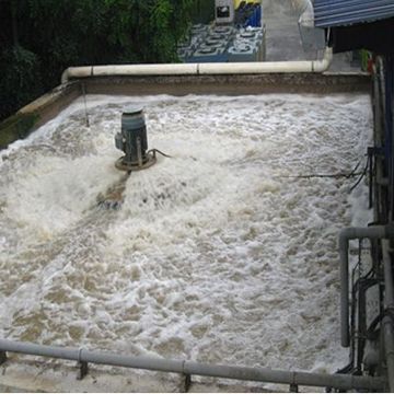 Foamy wastewater churning in a concrete basin with a central pump and pipes at the edges