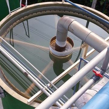 Top-down view of white industrial pipes over calm green water in a circular tank