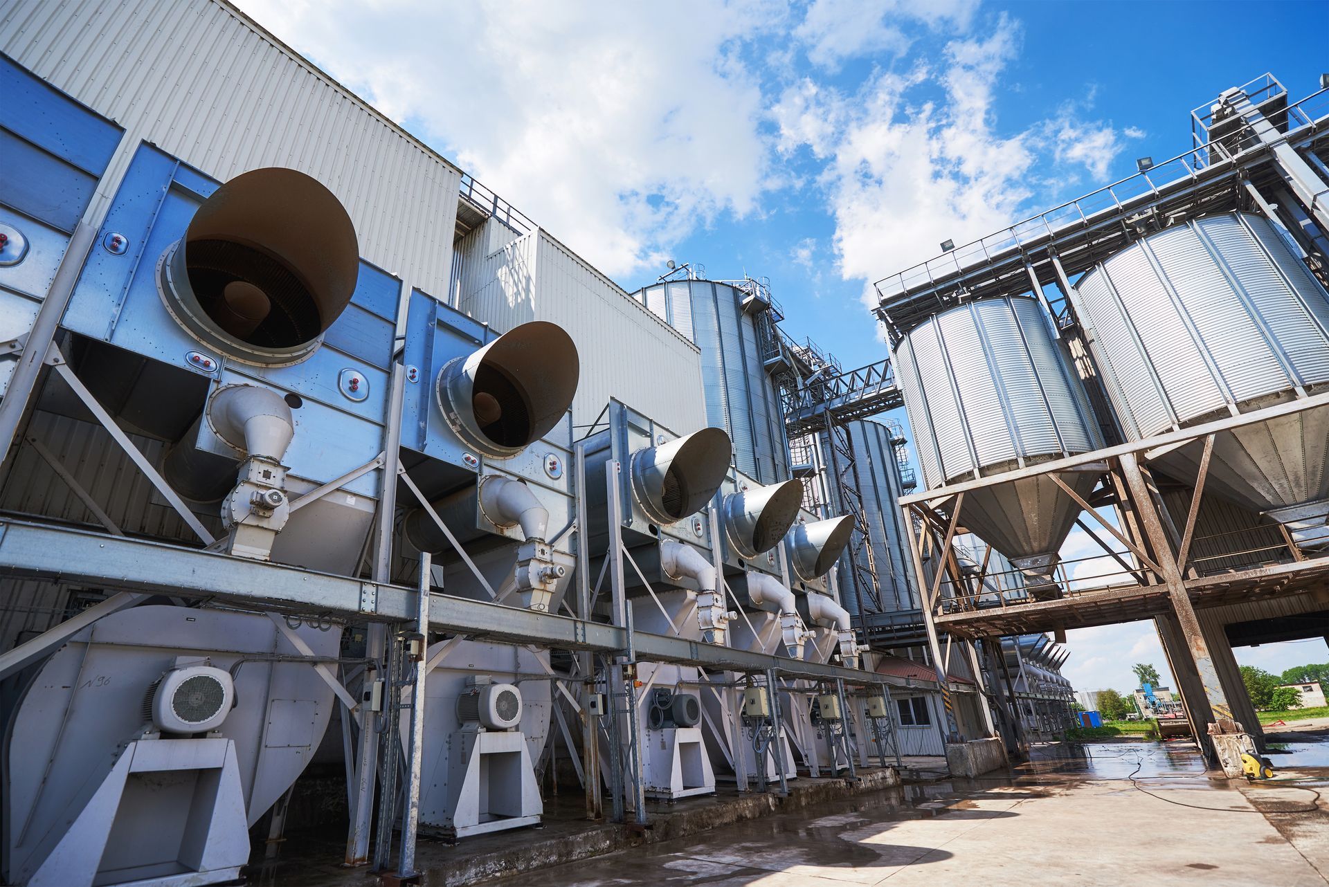 Industrial cooling units and metal ductwork outside a large blue factory building under a clear sky.