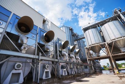 Industrial rooftop HVAC units and large ventilation fans beside a metal structure under a blue sky
