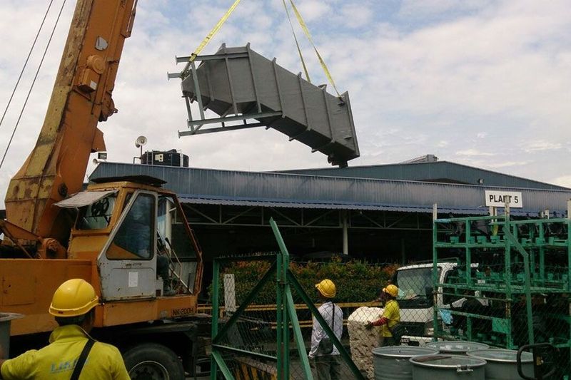 Crane lifting a large metal unit at a construction site with workers in hard hats nearby