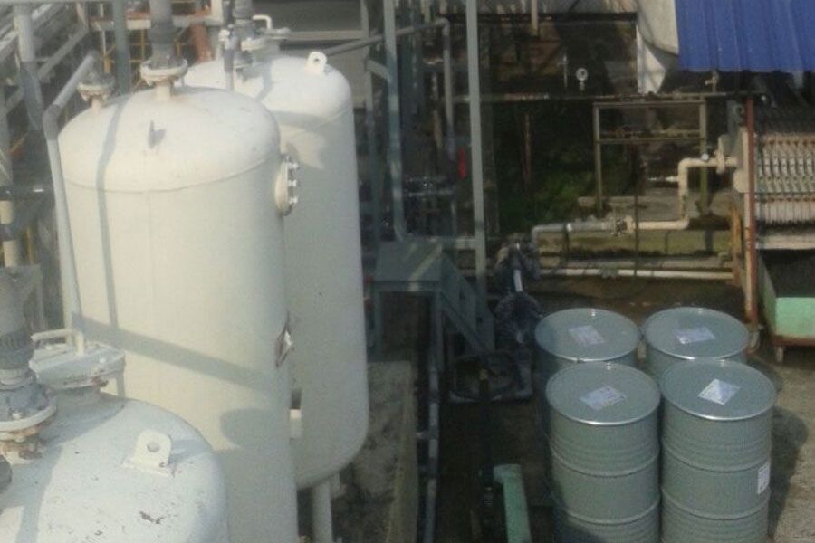 Industrial storage tanks and metal barrels in a factory yard, with pipes and equipment nearby