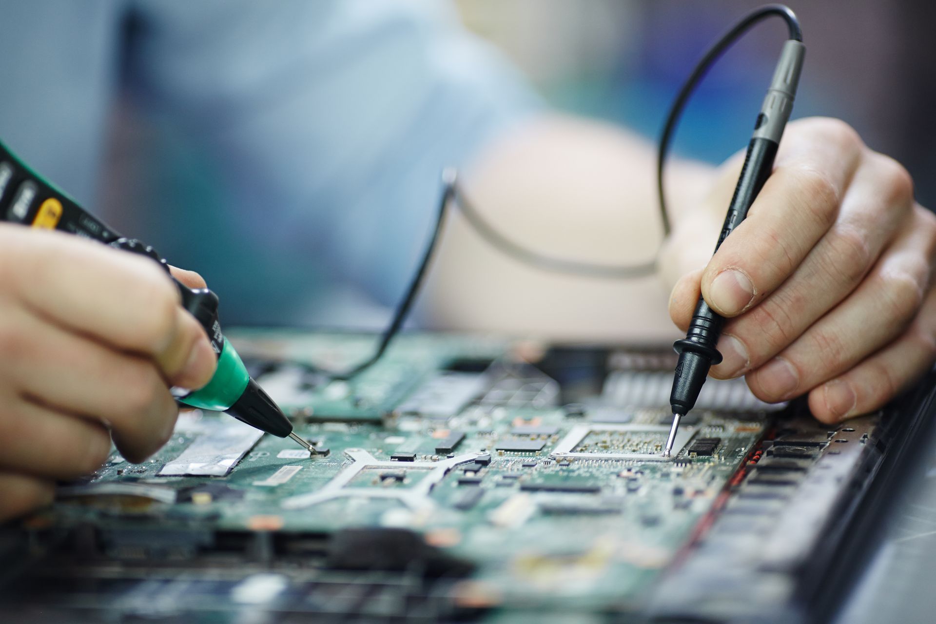 Hands using probes to inspect a circuit board during electronics repair