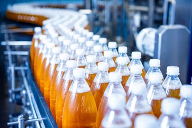 Rows of orange soda bottles with white caps moving along a bottling conveyor line
