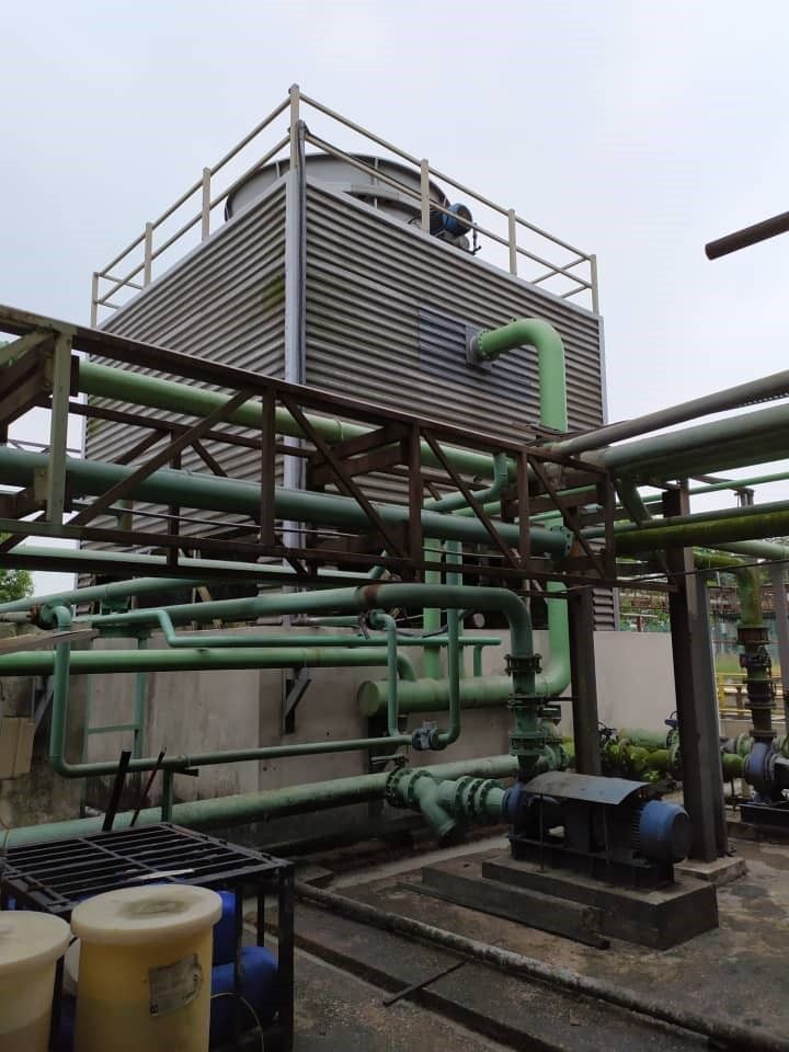 Industrial rooftop cooling equipment with green pipes and a metal tower under a cloudy sky