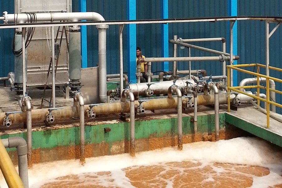 Industrial wastewater treatment tanks with pipes and foamy brown water beside a blue building