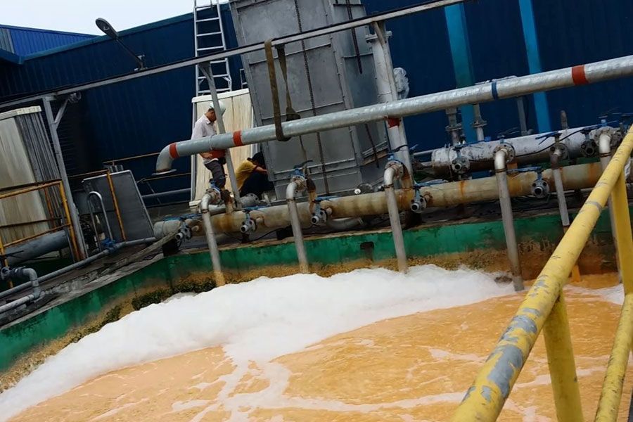 Industrial tank with foamy orange liquid and pipes, with a worker standing on a platform above it